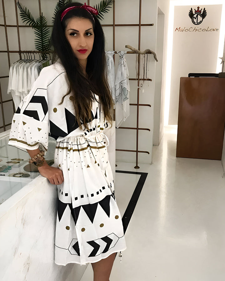 Femme portant un kimono blanc à motifs géométriques noirs et or. Style bohème chic, disponible chez MaloChicoLove. Collection de kimonos de créateurs. Mode estivale, robes légères.