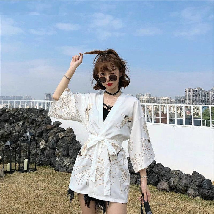 Femme portant un kimono blanc à motifs de grues dorées. Kimono tendance pour femme. Vêtements de style japonais. Notre collection de kimonos.