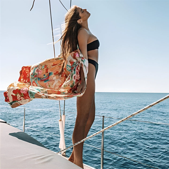 Femme en bikini sur un bateau, portant un kimono fleuri. Mer bleue en arrière-plan. Kimonos tendances pour l'été.