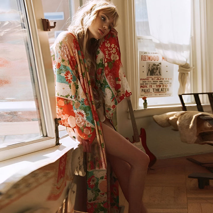 Femme rêveuse assise près de la fenêtre, portant un kimono floral coloré. Vêtements de style japonais pour femmes. Boutique en ligne de kimonos.