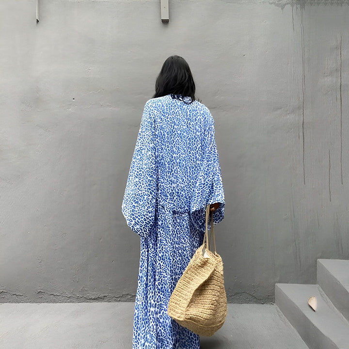 Femme vue de dos portant un kimono long bleu à motif léopard et un sac en paille. Découvrez notre collection de kimonos uniques et élégants.