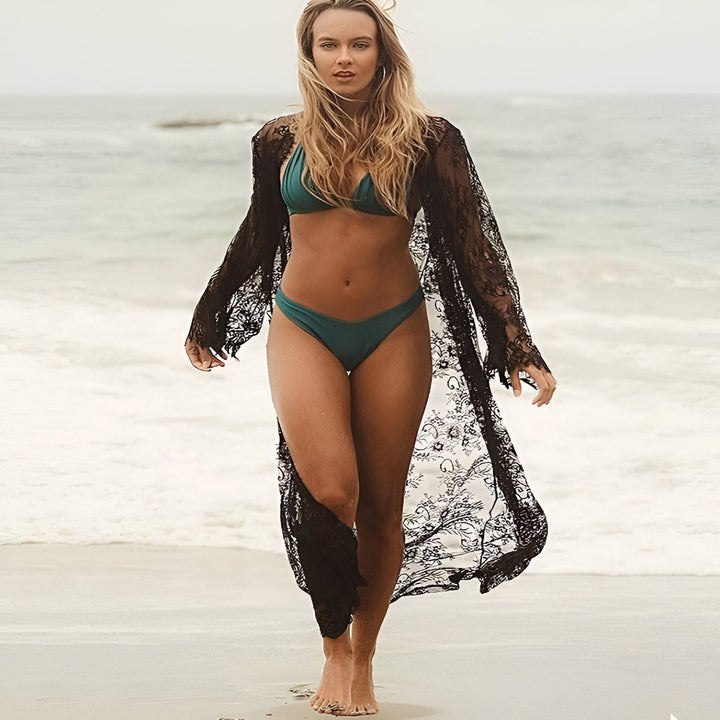 Femme en bikini vert émeraude et kimono long en dentelle noire sur la plage. Élégance et style décontracté. Découvrez notre collection de kimonos de plage!