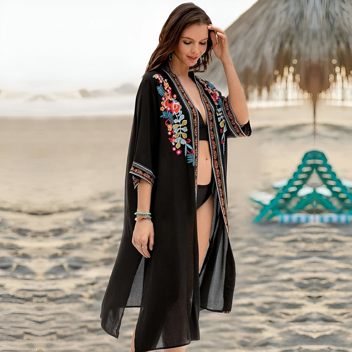 Femme portant un kimono noir brodé à fleurs sur une plage. Vêtement de plage tendance et élégant, parfait comme couverture de maillot de bain. Kimonos disponibles à l'achat.