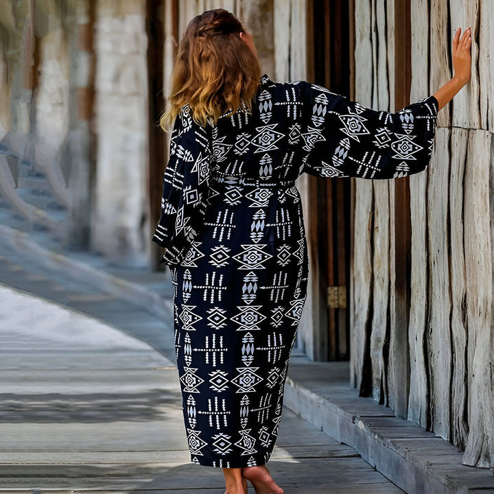 Femme portant un kimono long noir et blanc à motifs géométriques. Vêtement ample ceinturé, manches larges. Idéal pour se détendre avec style. Découvrez notre collection de kimonos uniques!