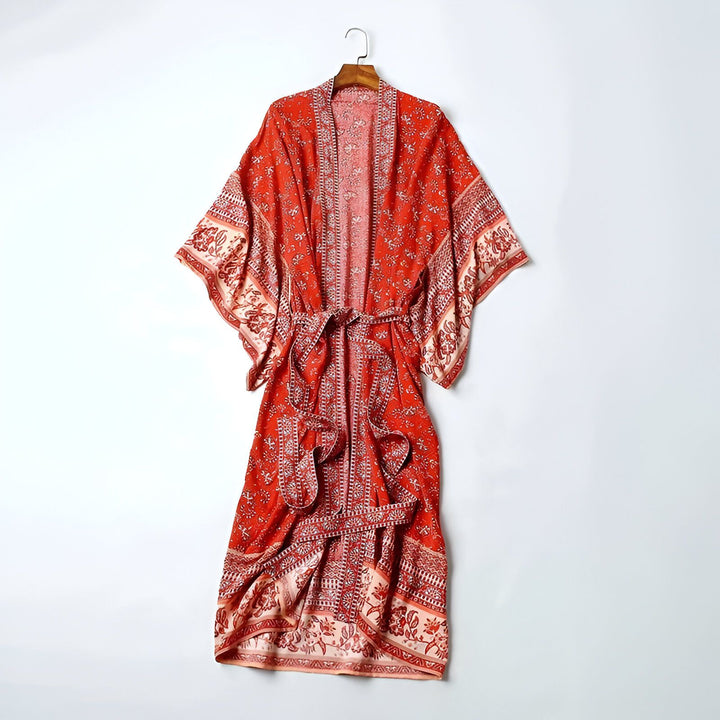 Kimono rouge fleuri, suspendu sur un cintre. Vêtement ample à manches larges, idéal comme peignoir ou veste légère. Style bohème chic pour toutes occasions.