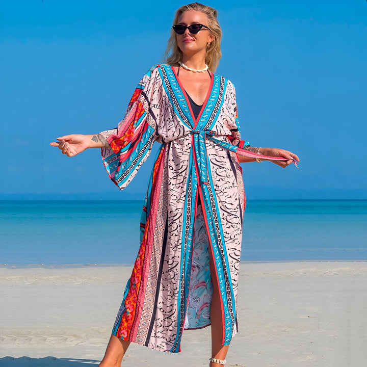 Femme portant un kimono long et coloré sur une plage ensoleillée. Kimono fleuri parfait pour l'été. Découvrez notre collection de kimonos pour femmes.