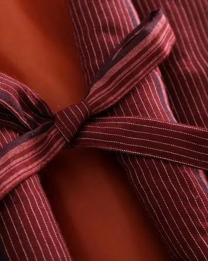 Détail d'un kimono à rayures bordeaux et blanches avec une ceinture nouée. Fermeture élégante d'un vêtement traditionnel japonais. Découvrez notre collection de kimonos uniques.