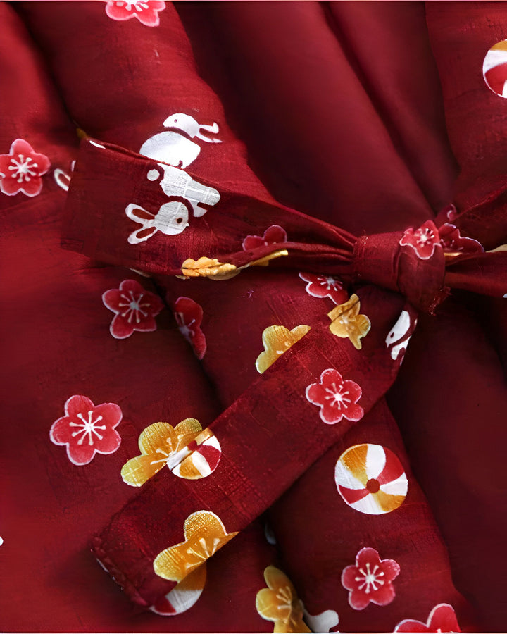 Détail d'un kimono rouge bordeaux avec motifs floraux et lapins blancs. Tissu noué avec une ceinture à motifs assortis. Vêtements japonais traditionnels en vente.