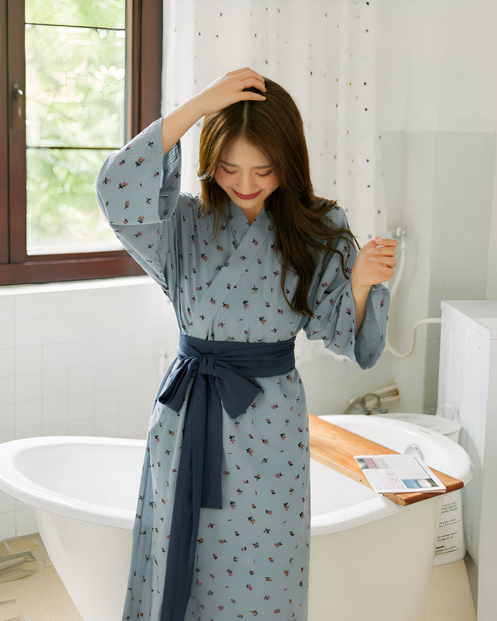 Femme souriante portant un kimono bleu à motifs floraux avec ceinture bleue dans une salle de bain. Vêtements de détente d'inspiration japonaise.