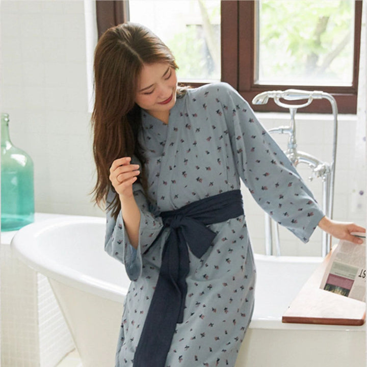 Femme portant un kimono bleu à motifs floraux dans une salle de bain. Peignoir japonais confortable avec ceinture nouée. Idéal pour se détendre après le bain. Kimonos de qualité disponibles à l'achat.