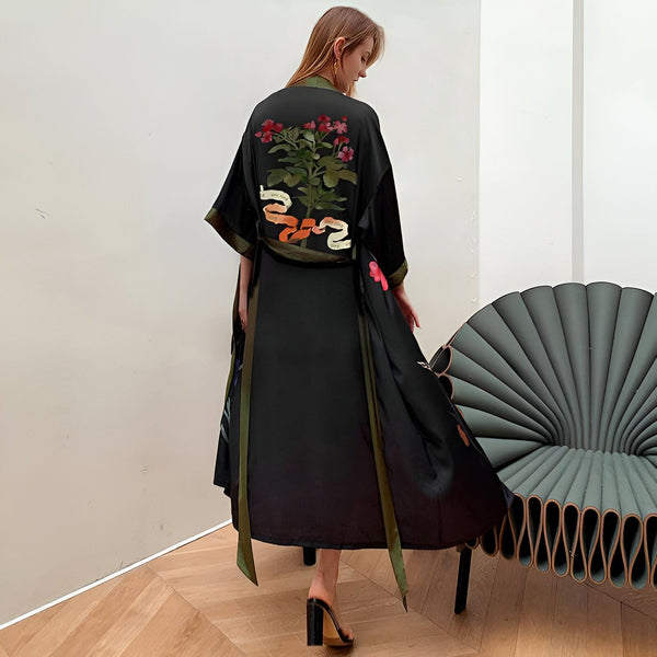 Femme portant un kimono noir long avec broderie florale sur le dos et ceinture verte. Élégant vêtement d'intérieur, style japonais revisité. Boutique de kimonos en ligne.