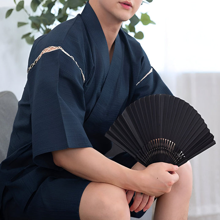 Homme portant un kimono bleu marine et tenant un éventail noir. Découvrez notre collection de kimonos japonais.