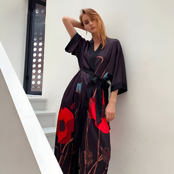 Femme portant un kimono noir à motifs floraux rouges et bleus, avec une ceinture noire nouée. Kimono élégant et confortable, parfait pour la détente à la maison ou une soirée spéciale.