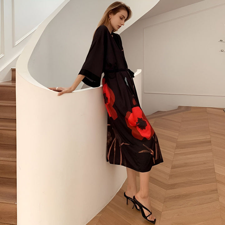Femme portant un kimono noir à motifs floraux rouges, adossée à un escalier blanc. Vente de kimonos en ligne. Style japonais moderne. Mode féminine confortable et élégante.