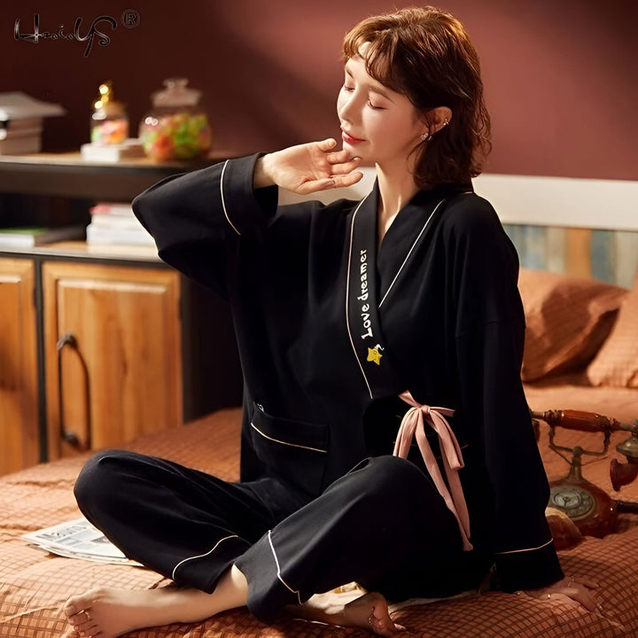 Femme assise portant un kimono noir avec inscription "Love dreamer" et bordure rose pâle. Vente de kimonos pour femmes en ligne. Kimono confortable et élégant.