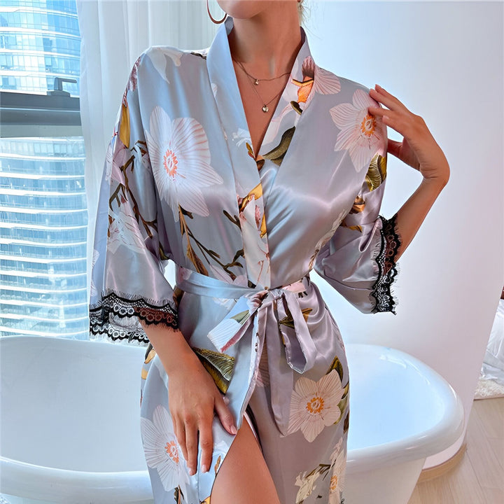 Femme portant un kimono en satin bleu clair à motifs floraux, manches courtes bordées de dentelle noire. Ceinture nouée. Kimono élégant disponible à l'achat.