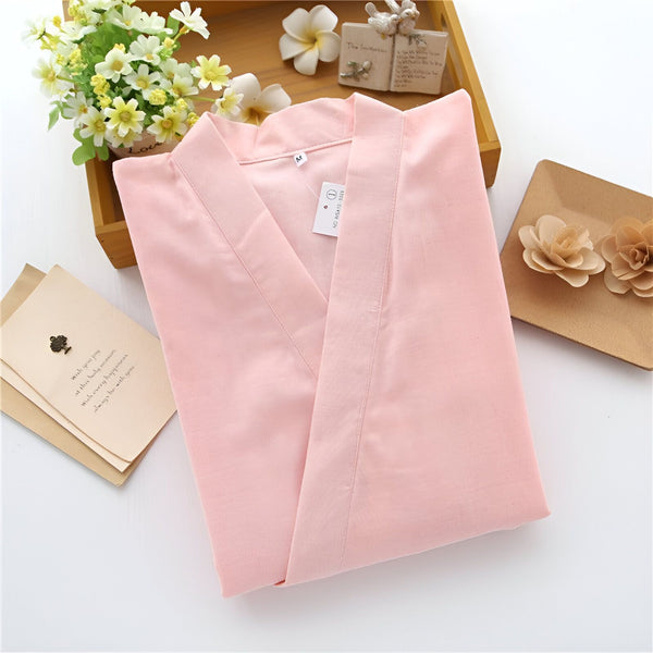 Kimono rose clair plié, présenté avec des fleurs décoratives et des cartes. Vêtements japonais traditionnels à vendre.