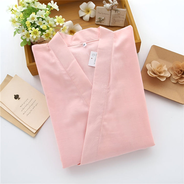 Kimono rose clair plié, présenté avec des fleurs décoratives et des cartes. Vêtements japonais traditionnels à vendre.