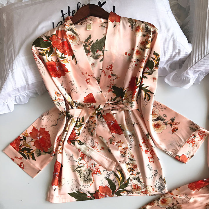 Kimono en satin rose pâle avec motif floral rouge et vert. Peignoir japonais élégant, idéal pour la détente à la maison. Vêtement d'intérieur confortable et raffiné.