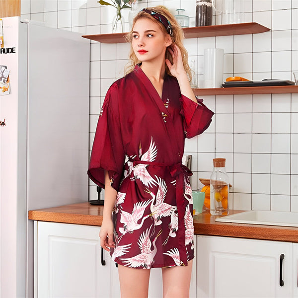 Femme portant un kimono bordeaux avec motifs de grues blanches dans une cuisine. Vente de kimonos, vêtements de détente, peignoirs japonais.