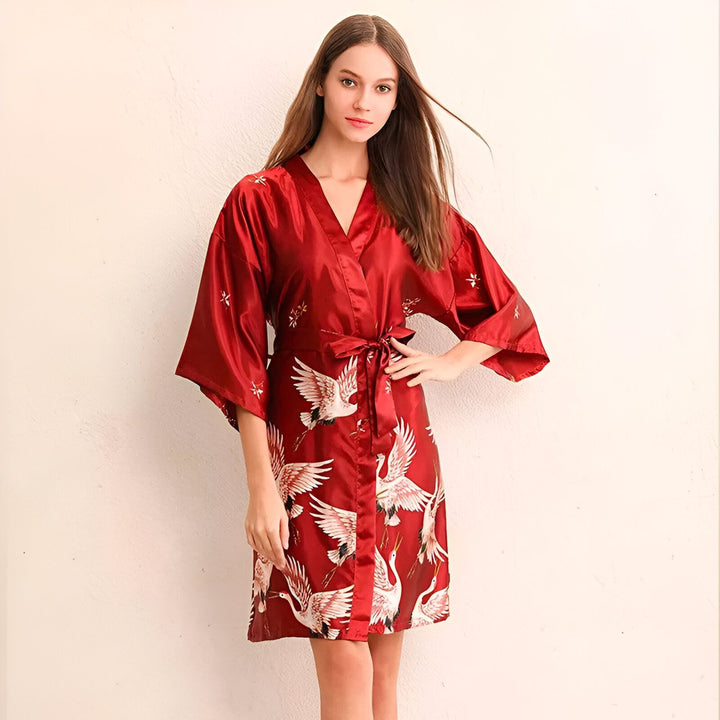 Femme portant un kimono rouge en soie avec des motifs de grues blanches. Vêtements de détente japonais traditionnels.