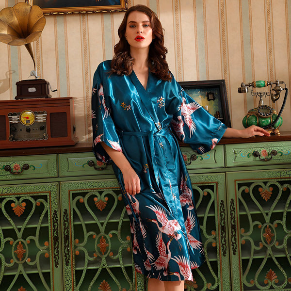 Femme portant un kimono bleu en satin avec des motifs de grues. Kimono de luxe, vêtement d'intérieur élégant. Collection de kimonos pour femmes.