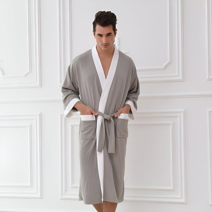Homme portant un kimono gris avec bordures blanches. Vêtement d'intérieur confortable et élégant, idéal après le bain ou pour se détendre à la maison. Découvrez notre collection de kimonos pour hommes.