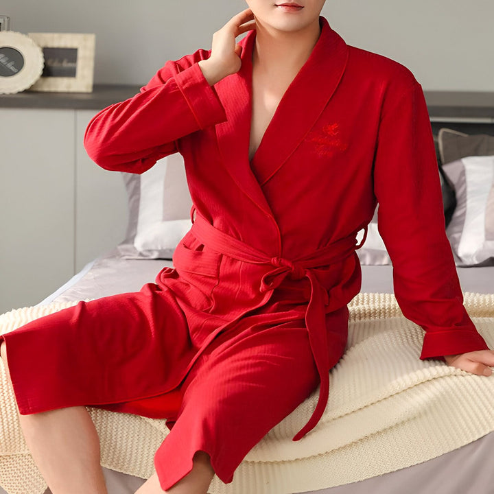Homme portant un kimono rouge, assis sur un lit. Peignoir japonais en coton pour homme, confortable et élégant. Idéal pour se détendre à la maison.