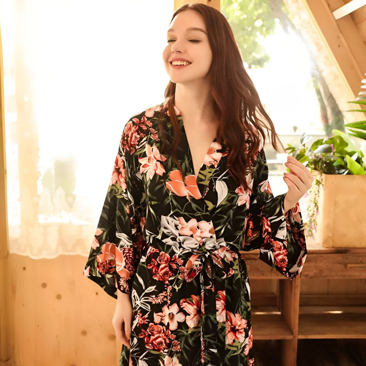 Femme souriante portant un kimono noir à motifs floraux colorés. Kimono élégant et confortable, parfait pour la détente ou comme vêtement d'intérieur chic. Notre collection de kimonos offre une variété de styles et d'imprimés.