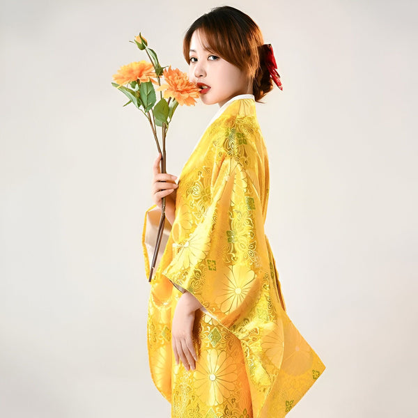 Femme en kimono japonais jaune fleuri tenant des fleurs orange. Vente de kimonos traditionnels et modernes pour femmes. Style élégant et raffiné.