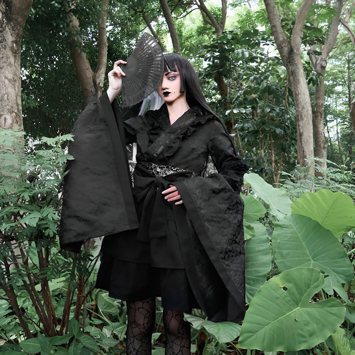 Femme portant un kimono noir gothique avec un éventail, dans une forêt. Kimono élégant et sombre, idéal pour un style unique. Découvrez notre collection de kimonos.