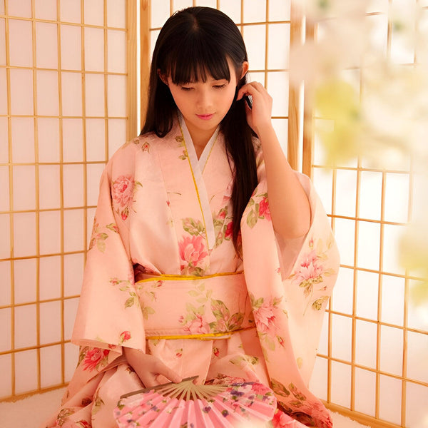 Jeune femme en kimono rose à motifs floraux tenant un éventail. Kimono traditionnel japonais disponible à l'achat. Mode et culture japonaises.