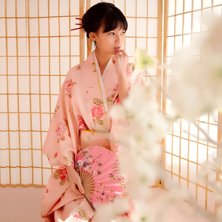 Jeune femme en kimono rose à motifs floraux, tenant un éventail assorti. Vente de kimonos japonais traditionnels.