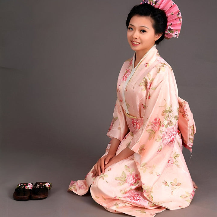 Jeune femme en kimono rose à motifs floraux, agenouillée avec des geta à côté. Découvrez notre collection de kimonos traditionnels et modernes.