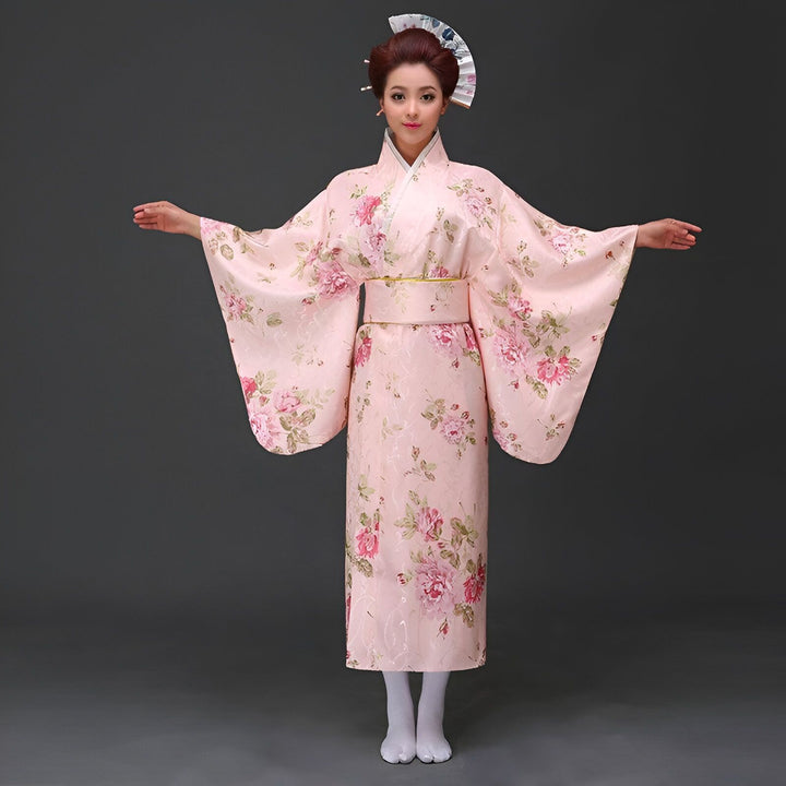 Femme en kimono rose à motifs floraux, coiffée avec un éventail, bras ouverts. Vente de kimonos japonais authentiques et élégants.
