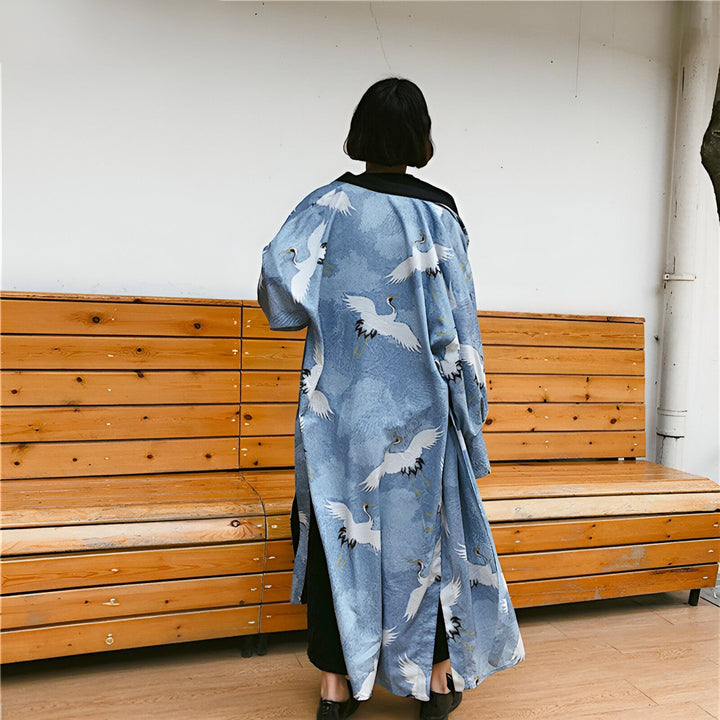 Femme de dos portant un kimono long bleu ciel à motifs de grues blanches. Vêtement de style japonais, idéal pour un look tendance et original. Kimonos disponibles à l'achat.