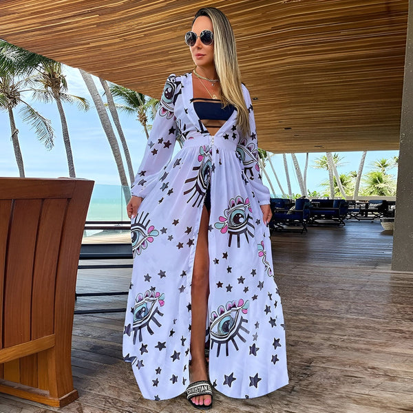 Femme portant un kimono blanc long avec des motifs d'yeux et d'étoiles, devant une plage tropicale. Vente de kimonos originaux.