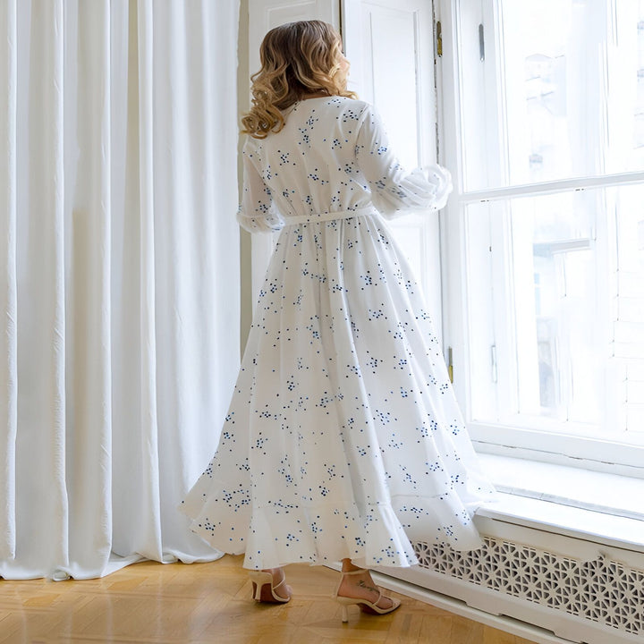 Femme portant un kimono blanc à motifs bleus, regardant par la fenêtre. Kimono élégant pour toutes les occasions. Découvrez notre collection de kimonos uniques.