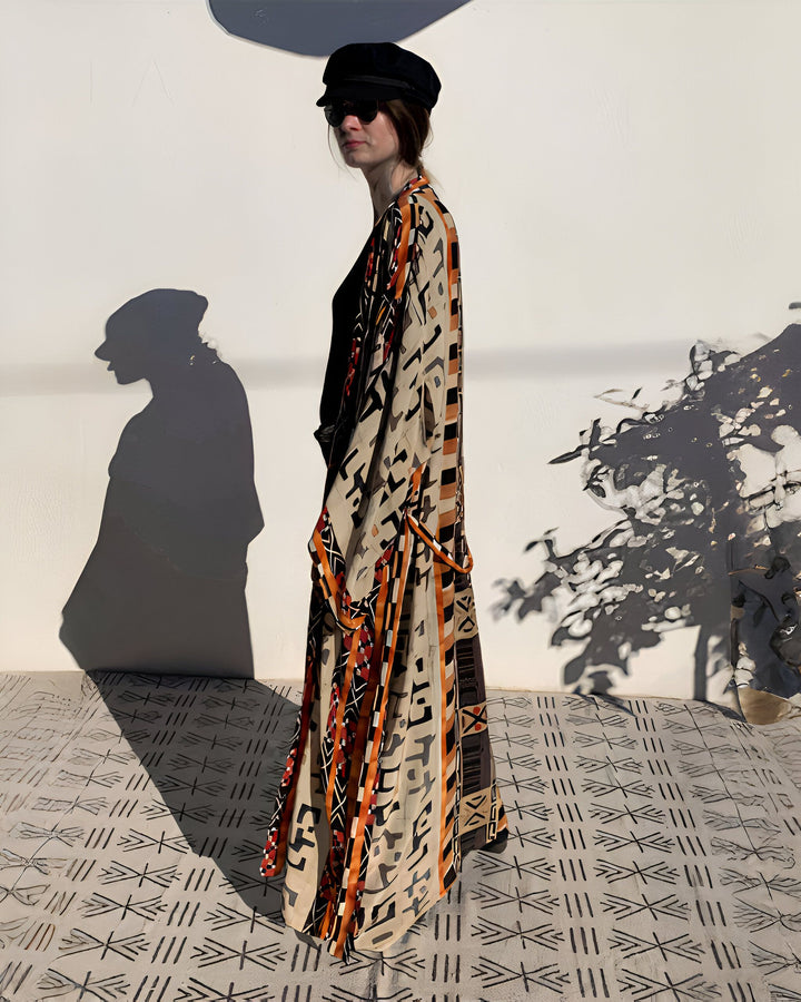 Femme portant un kimono long à motifs ethniques orange et noir. Elle porte un chapeau et des lunettes de soleil. Vente de kimonos.