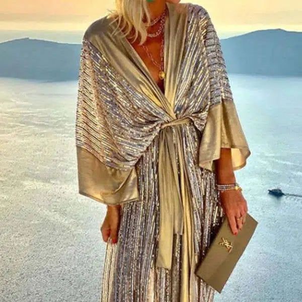 Femme portant un kimono doré scintillant avec une pochette assortie devant un paysage marin. Kimonos élégants et robes de chambre disponibles.