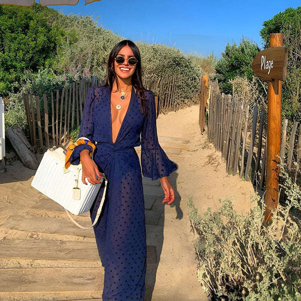 Femme souriante portant un kimono bleu à pois, avec un panier blanc, sur un chemin de plage ensoleillé. Élégance décontractée pour une journée d'été. Vêtements style kimono en vente.