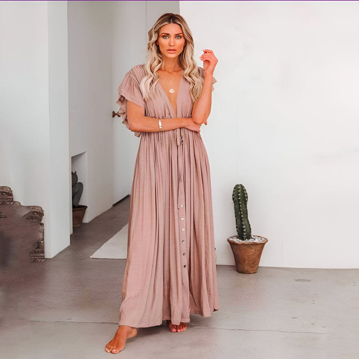 Femme blonde portant une longue robe style kimono couleur pêche avec col en V et boutons. Détails à volants aux manches. Parfait pour un look décontracté et élégant.