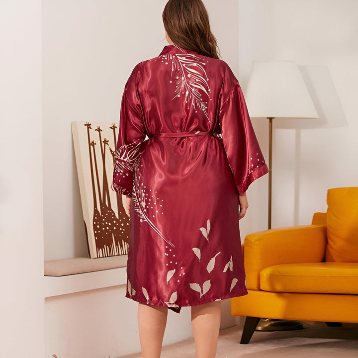 Femme portant un kimono bordeaux en satin avec motifs de plumes blanches, vue de dos. Vêtement d'intérieur élégant et confortable, idéal pour la détente et le cocooning. Kimonos de haute qualité en vente.