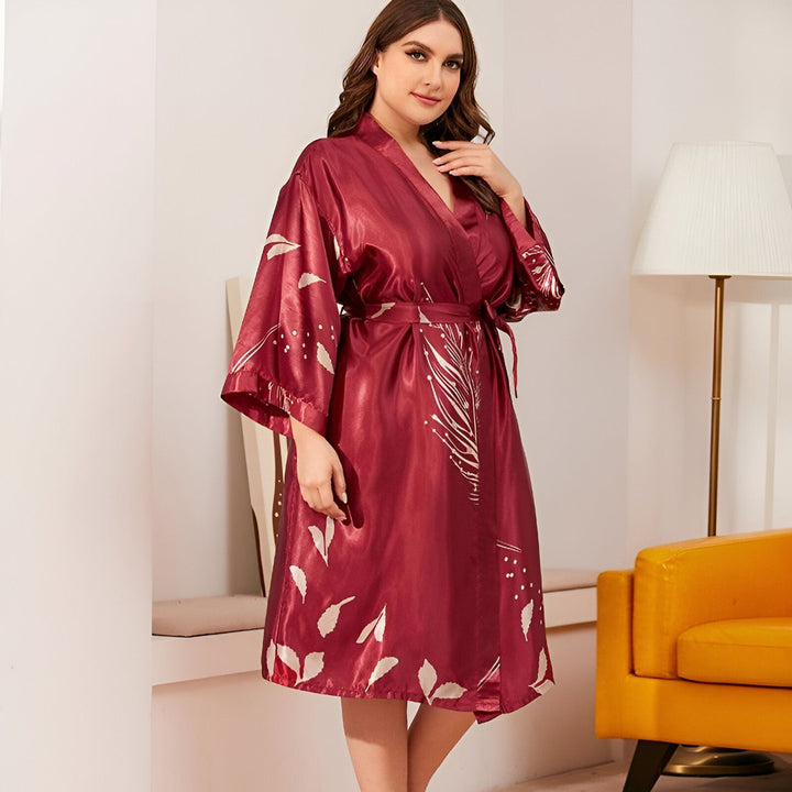 Femme portant un kimono bordeaux avec des motifs de feuilles. Peignoir élégant en soie, parfait pour se détendre à la maison. Découvrez notre collection de kimonos confortables et raffinés.