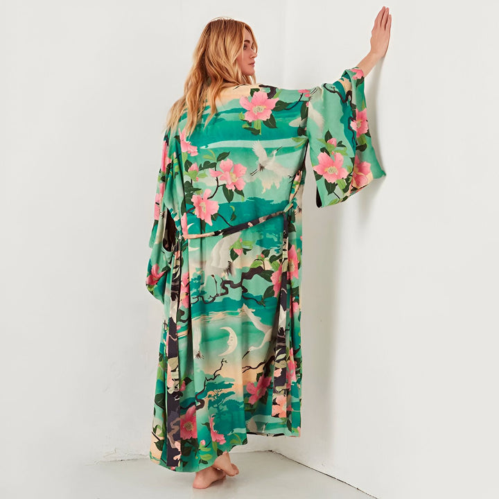 Femme portant un kimono long vert avec motif floral et grues. Vêtement de détente élégant. Kimonos à motifs uniques en vente.
