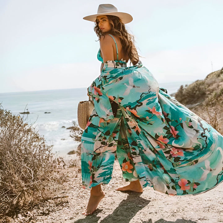 Femme portant un kimono turquoise à motifs floraux et d'oiseaux sur une plage ensoleillée. Chapeau de paille et panier en osier. Mode plage, kimono, vêtements d'été.