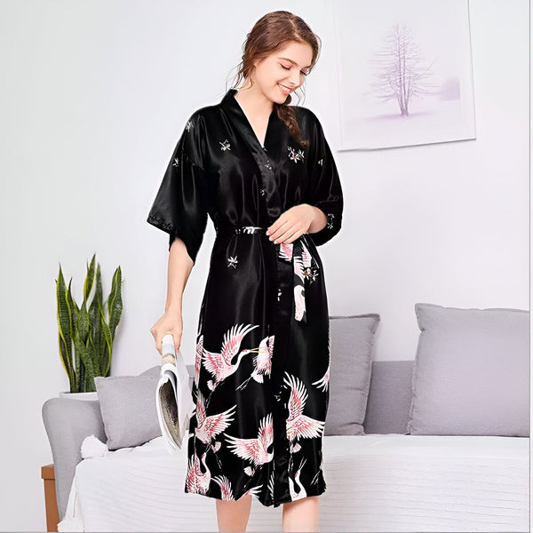 Femme souriante portant un kimono noir en soie avec motifs de grues. Peignoir japonais élégant avec ceinture assortie. Vente de kimonos en ligne.