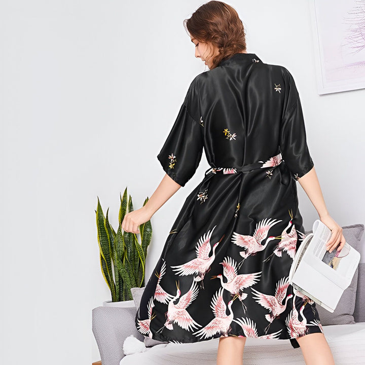 Femme portant un kimono noir avec des motifs de grues roses et blanches. Vente de kimonos en ligne.