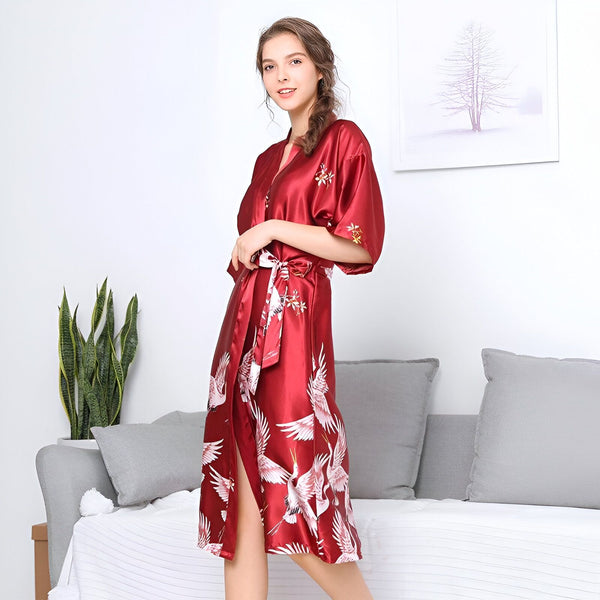 Femme portant un kimono rouge en satin avec des motifs de grues blanches. Kimono élégant et confortable, parfait pour se détendre à la maison. Découvrez notre collection de kimonos uniques !