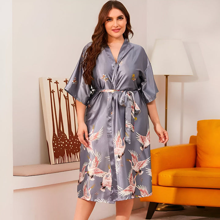 Femme portant un kimono gris à motifs de grues roses. Vente de kimonos pour femmes en ligne. Kimono en soie confortable et élégant. Idéal pour se détendre à la maison ou comme vêtement d'extérieur léger.